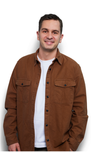 Smiling man in a brown jacket and white shirt, standing against a white background. Casual attire, friendly expression.