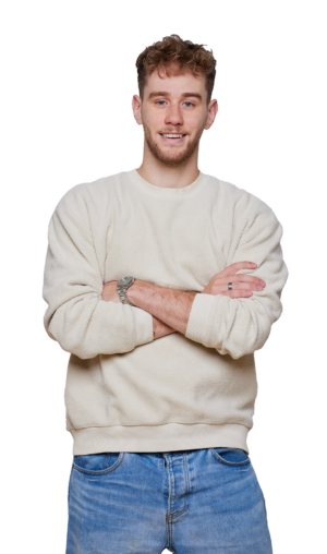 Smiling person in a light-colored sweater and jeans, arms crossed, against plain white background. Casual clothing and style.