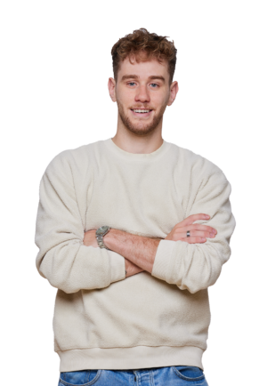 Smiling person in a light-colored sweater and jeans, arms crossed, against plain white background. Casual clothing and style.